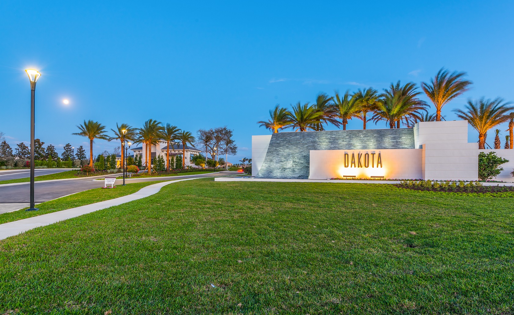 Dakota community entrance monument illuminated at dusk, lined with palm trees
